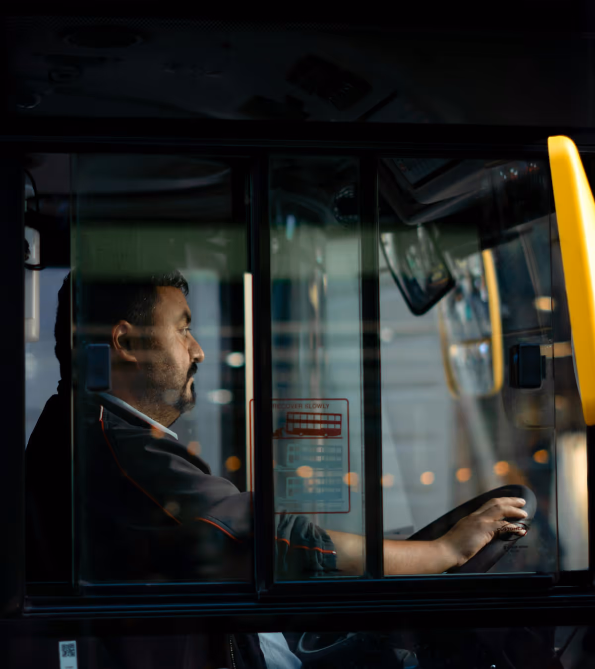 Side view of a focused male bus driver holding the steering wheel inside a bus driver's cabin.